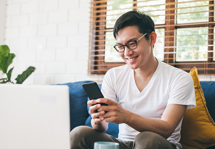 Man with glasses sitting on a couch looking at his finances on his phone