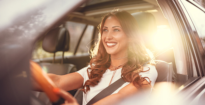 A smiling member is seen driving their car during the day.