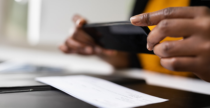 A member is taking a photo of a check on their desk with their mobile phone.
