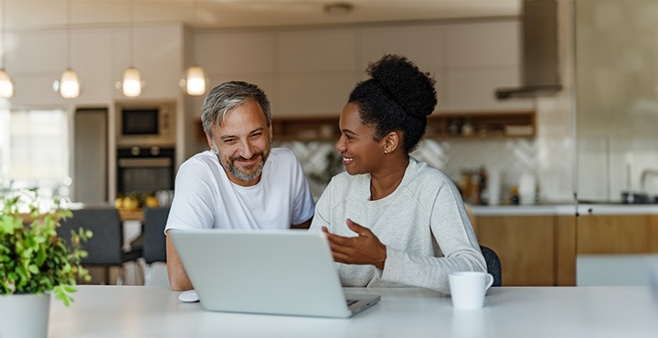 Smiling couple sitting at a table in their home, working together on retirement planning.