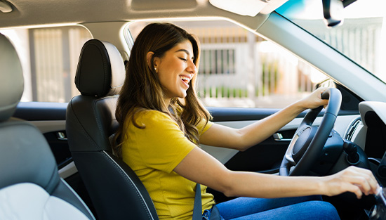 A cheerful woman in a yellow shirt interacting with the dashboard touch screen of a modern vehicle.