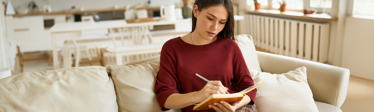 A new homeowner is on their couch writing down a list of items that they need for their new home.