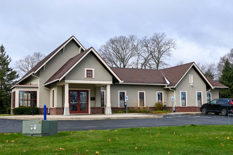 Exterior view of Grafton branch - parking lot in the foreground of building with light brown siding surrounded by trees.
