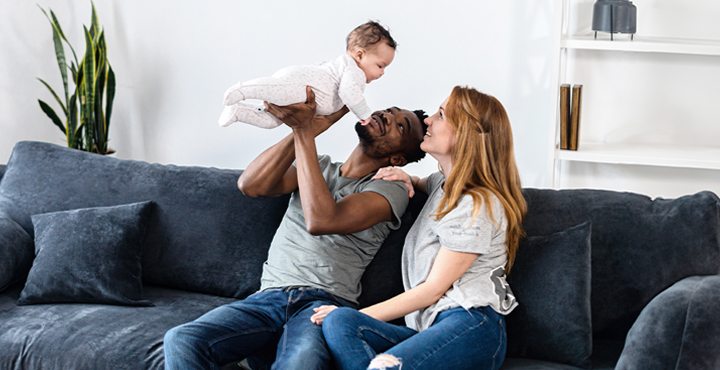 Couple sitting on couch holding their baby up in the air