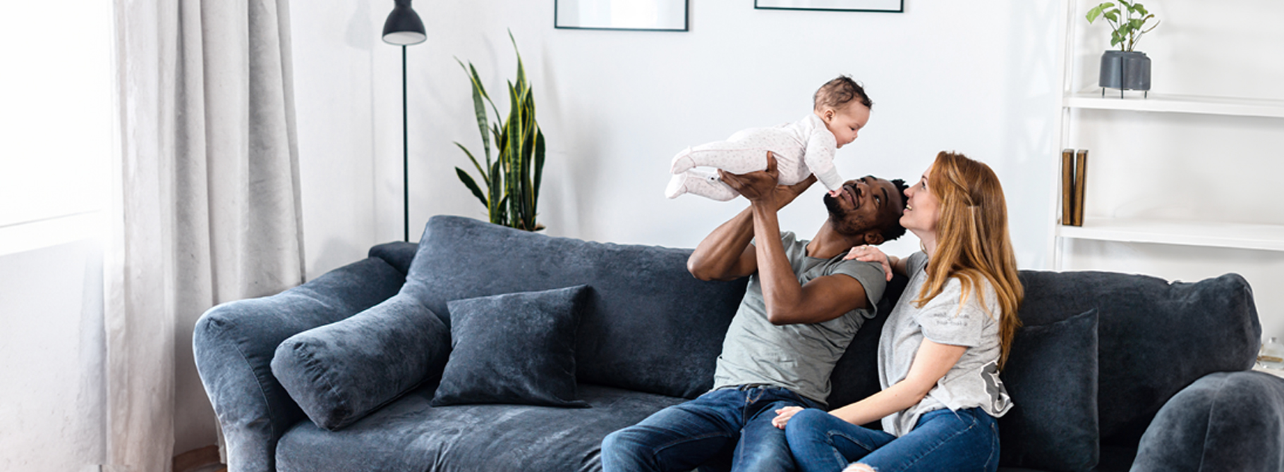 Couple sitting on couch holding their baby up in the air
