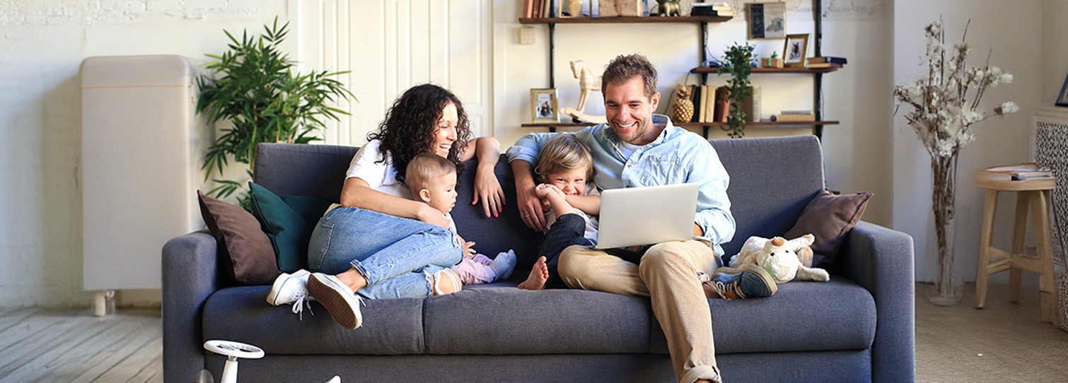 Happy couple on couch with their children laughing at something on their laptop.
