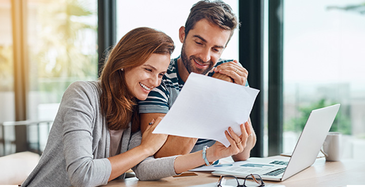 An excited couple sits at their dining room table as they read tips on saving up for their wedding day.