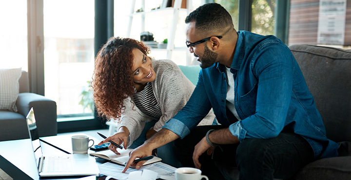 Smiling couple sitting at a table in their home, working together on retirement planning.
