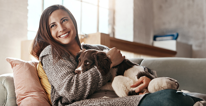 Happy first-time homebuyer sitting on the couch with her dog, enjoying a moment of relaxation.